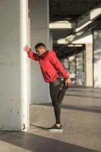 male in red jacket stretching leg against wall