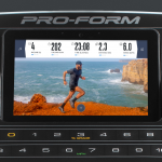 Console screen of the ProForm Pro 9000 treadmill with an image of a man in athletic attire running alongside a mountain with a view of the ocean behind him. The treadmill features a fan, several buttons and a speaker
