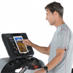 A fit man in athletic attire walking on the Landice L7 Treadmill setting up his workout on the screen