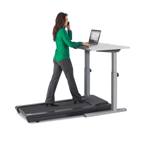 A lady in business casual attire walking on the TR1200 treadmill desk while being on the phone and working on a laptop.